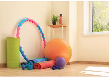 Bola, colchonete, halteres e bambolê em um espaço iluminado para exercícios.