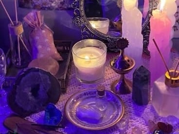 A mystical spiritual altar with lit candles, incense, crystals, and a vintage mirror under purple lighting.