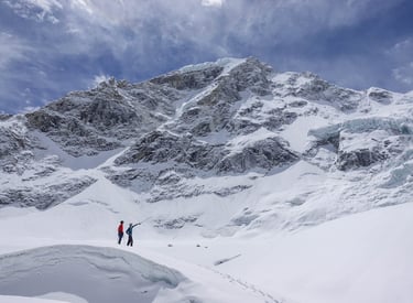 two people standing in the snow near a mountain