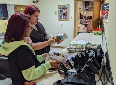 Two student hairstylists review beauty magazines and brochure inside cosmetology school..
