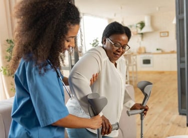 A woman using crutches stands beside another woman using a walker, both smiling in a supportive envi