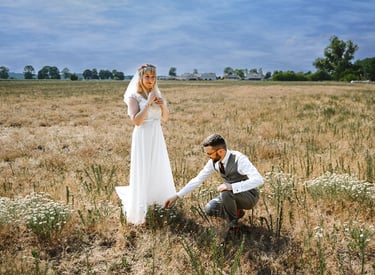 Dieses Farbfoto zeigt ein Brautpaar in einem trockenen Feld unter einem dramatischen Himmel. Die Braut steht in einem weißen