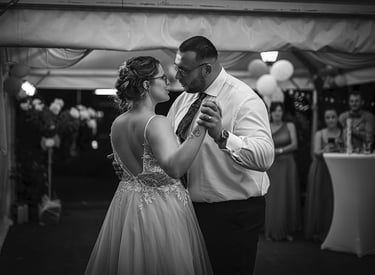 Ein Schwarz-Weiß-Foto eines Brautpaares, das bei seiner Hochzeit tanzt, wobei die Braut ein rückenfreies Kleid trägt und der