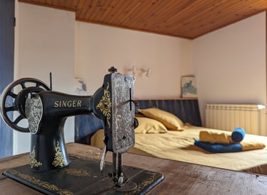 Une machine à coudre singer et en arrière plan un lit avec des draps dorés