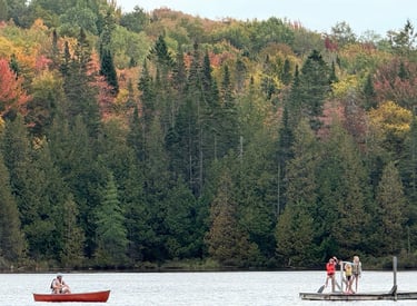 Three kids on a raft in the middle of a Vermont lake as their father looks on from a nearby canoe
