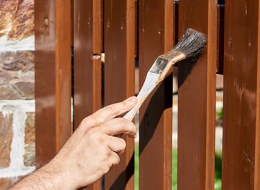 Une personne applique une protection pour bois sur une clôture de jardin et un portail