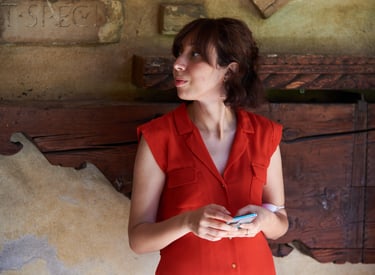 Persona con vestito rosso estivo e smartphone davanti a muro rustico in Museo