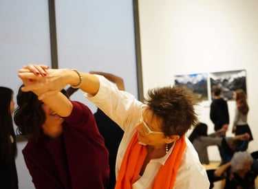 Giovane e anziana danzano insieme tenendosi per mano in museo, sullo sfondo altri danzano come loro