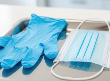 Blue disposable gloves and a surgical face mask placed on a metal tray in a clinical setting