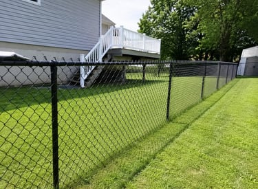 Black vinyl-coated chain link fence installed in a residential backyard with a green lawn and white deck.