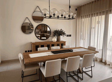 Comedor con mobiliario cálido, espejos decorativos y una lámpara lineal como pieza central | KARÄNA