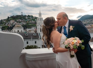 El novio besando a la  novia mientras la agarra de la cintura en un terraza con vista al Panecillo en el centro histórico 