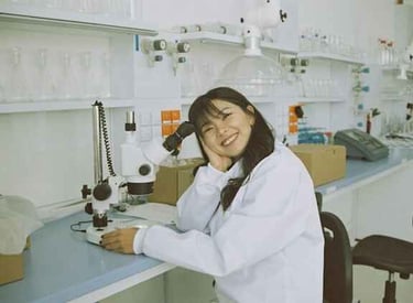 female in lab coat sitting at a desk and using a scientific microscope