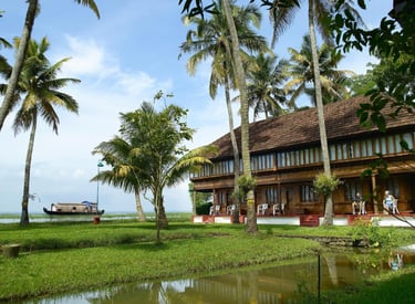Traditional Kerala house surrounded by palm trees and lush greenery, overlooking tranquil backwaters.