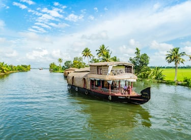 Houseboat cruising through Kerala's backwaters, surrounded by lush palm trees and vibrant greenery under a blue sky.