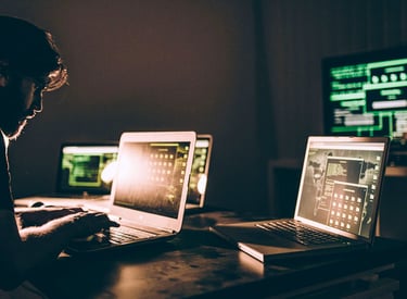 a man sitting at a desk with two laptops