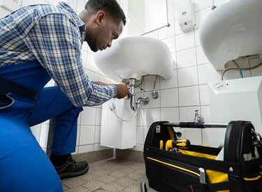 A professional plumber in London repairing a sink in a tiled bathroom, with a toolbox full of plumbi