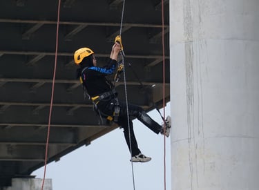 Professional bridge inspector rappelling on ropes to perform maintenance on a concrete pillar.