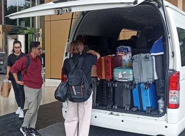Satu orang pria dua orang wanita sedang menurunkan bagasi dari Hiace.