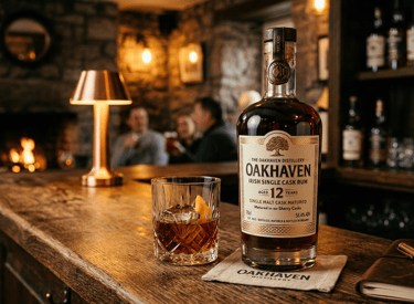 A bottle of Oakhaven 12 Year Irish Single Cask Rum and a crystal glass on a rustic wooden bar.