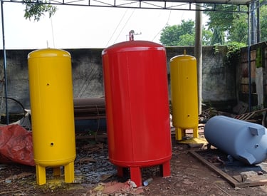 Industrial air compressor receiver tanks in red and yellow at a manufacturing workshop.