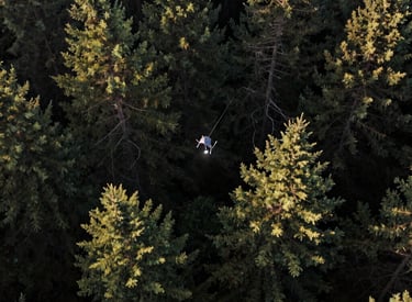 Drone flying over rugged mountain terrain at dawn with searchlights on.