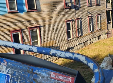 A blue scissor lift basket overlooks a residential building with weathered beige wood siding.
