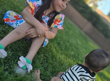 Una niña con vestido floral sentada sobre el césped verde sonríe a un bebé