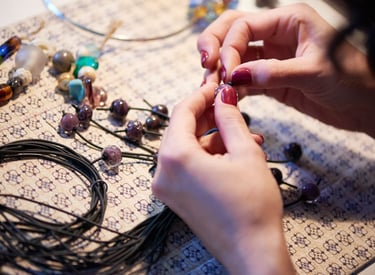 Artesano de joyería hecha a mano ensartando cuentas de vidrio moradas en un cordón negro para crear 