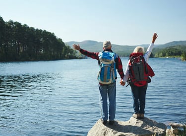 Una pareja de adultos mayores con mochilas haciendo senderismo junto a un lago de montaña