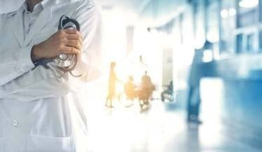 Un médico con una bata blanca de laboratorio sosteniendo un estetoscopio en un pasillo de hospital