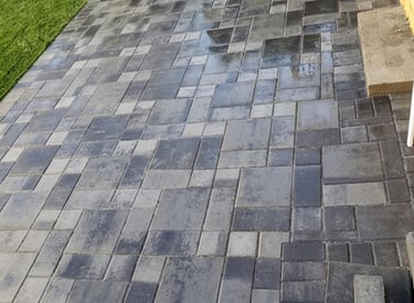 Backyard patio installation with interlocking grey stone pavers next to a lush green lawn, showcasin