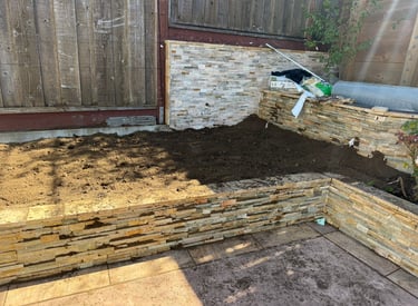 Raised garden bed featuring stacked stone retaining walls filled with fresh dark topsoil.