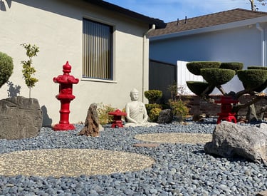 Zen garden with a Buddha statue, red Japanese lanterns, and blue river rocks for landscaping.