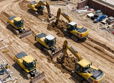 Construction site with heavy machinery moving earth under a cloudy sky.