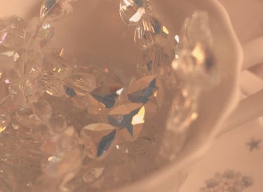 Elegant crystal beads and iridescent glass jewelry inside a vintage porcelain teacup with soft aesthetic lighting.