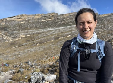 A smiling woman hiking with a backpack in a rocky mountain landscape under a blue sky.