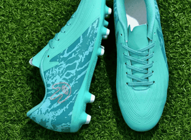 Botines de fútbol con estampado turquesa y tacos blancos, descansando sobre un vibrante césped.