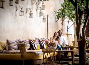 Smiling couple relaxing on a Moroccan-style lounge with colorful pillows and hanging lanterns.