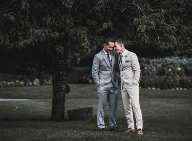 A happy groom couple in suits sharing a romantic moment during an outdoor wedding ceremony.