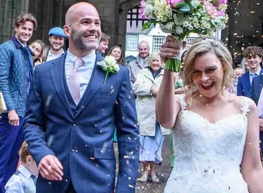 Smiling bride and groom celebrate under falling confetti during their outdoor wedding ceremony.