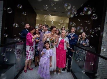 Wedding guests blow bubbles around a smiling bride and groom during a joyful exit celebration.