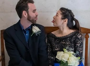 A playful bride and groom making funny faces while sitting together at their wedding venue.