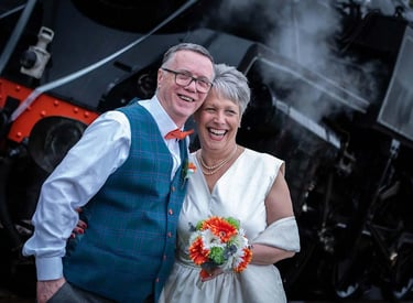 bride and groom standing in front of a steam train