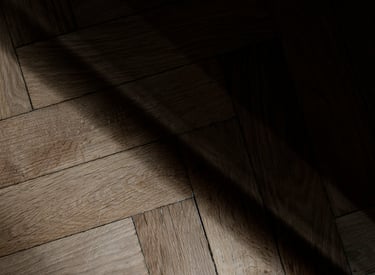 Rustic herringbone oak wood parquet flooring with natural texture and dramatic shadows.