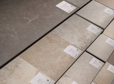 Display of various textured porcelain floor tiles in grey, beige, and stone finishes for home renovation.