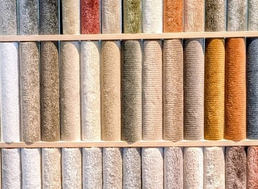 A colorful display of textured carpet samples and plush area rug rolls on a showroom wall.