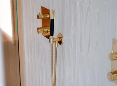 Luxury modern gold shower hardware and handheld sprayer mounted on white textured vertical subway tile.