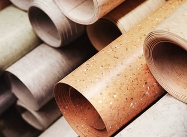 Stacked rolls of durable linoleum flooring in various neutral colors and patterns for home renovation.