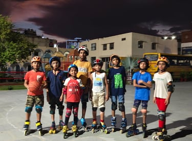 A group of young children wearing helmets and safety gear posing with roller skates on an outdoor rink at night.